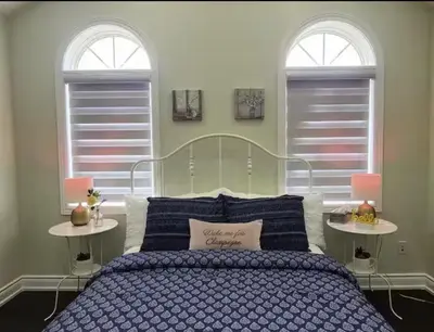 a bedroom with a blue bed with two windows at Lavish Bright Bedroom in Brampton