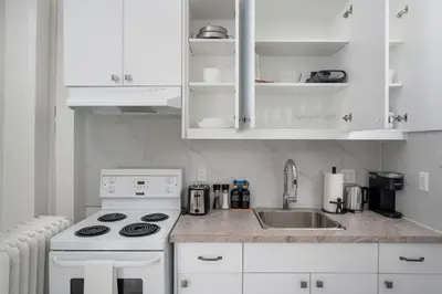a white kitchen with a stove and a sink at Stylish Roncesvalles Flat in Toronto