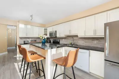 a kitchen with white cabinets and bar stools at House with 5 Beds for Families in Great Location in Mississauga