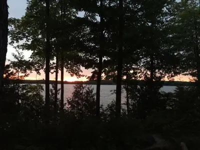 a sunset over a body of water with trees at Lake Eugenia Escape - Cozy Lakefront with Hot Tub in Flesherton