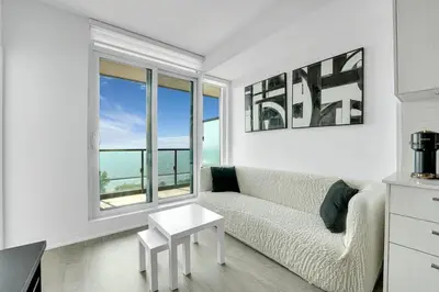 a living room with a couch and a table and windows at Beachside 2 Bedroom Suite with CN Tower, lake View, and Parking! in Toronto