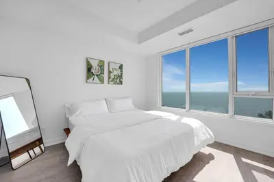 a white bedroom with a bed and large windows at Beachside 2 Bedroom Suite with CN Tower, lake View, and Parking! in Toronto