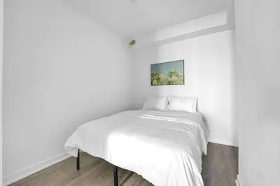 a white bedroom with a bed with white sheets at Beachside 2 Bedroom Suite with CN Tower, lake View, and Parking! in Toronto