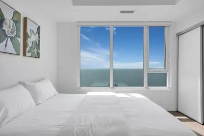 a white bedroom with a large bed and a large window at Beachside 2 Bedroom Suite with CN Tower, lake View, and Parking! in Toronto