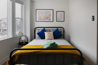 a bedroom with a bed with blue pillows and a window at Urban Oasis Steps to UofT Culture Patio in Toronto
