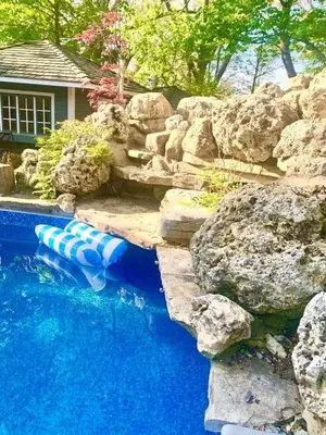 a pool with blue water and rocks in a yard at The Serenity Home Pool/Yoga/Game Room by the Lake in Mississauga