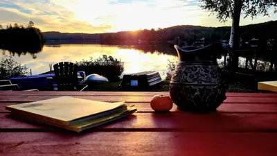 a book and a vase on a table with a view of a lake at Amazing Lakefront cottage on Paradise Lake in Haliburton