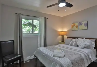 a bedroom with a bed with a ceiling fan and a chair at Cozy Georgian Bay Cottage Firepit, Beach, 4-Season in Tiny