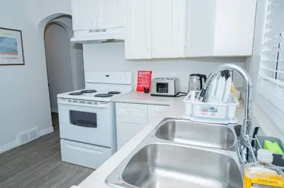 a white kitchen with a sink and a stove at Cozy Bungalow Near Niagara Falls - Perfect Family Retreat in Niagara Falls