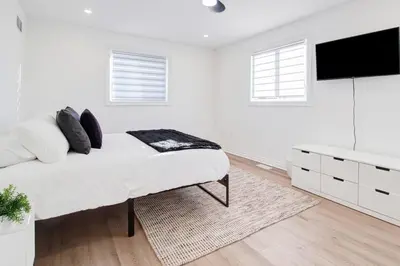 a white bedroom with a bed and a flat screen tv at Stylish 3BR Steps to Canal, Easy Drive to Falls in Port Colborne