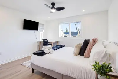 a white bedroom with a bed with a ceiling fan at Stylish 3BR Steps to Canal, Easy Drive to Falls in Port Colborne