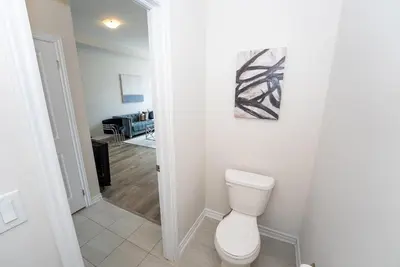 a white bathroom with a toilet and a living room at Modern Vaughan Retreat, 10 mins to Pearson Airport, Vaughan Mall in Vaughan