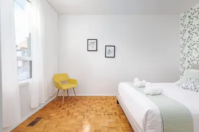 a white bedroom with a bed and a yellow chair at Charming 4 Bed Home + 2Parking in Toronto