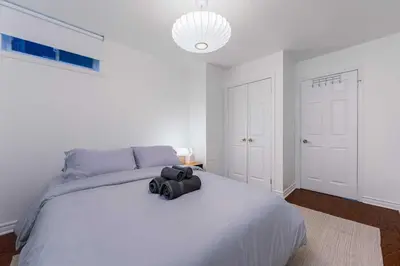 a white bedroom with a large bed with a black backpack on it at Contemporary 1BR Basement Suite with Private Entrance in Toronto