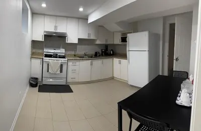 a kitchen with white cabinets and a table and a refrigerator at Private Deluxe basement suiteP1 in Mississauga