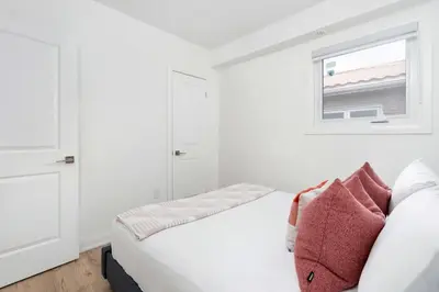 a white bedroom with a couch and a window at Chic 3BR Ossington Hub Near Subway & Shops in Toronto
