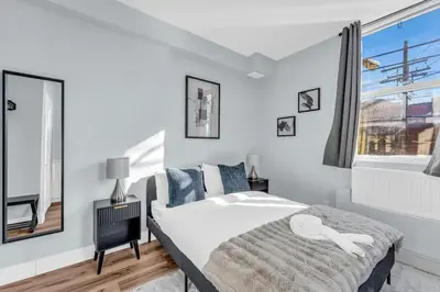 a white bedroom with a bed and a window at Guestic at Queen West in Toronto