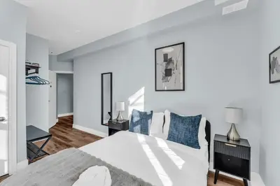 a white bedroom with a large bed with blue pillows at Guestic at Queen West in Toronto