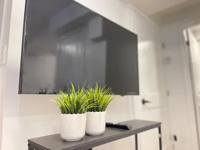 two white vases with plants on a table with a tv at The Scholar Suite Modern Comfort Near Western U in London