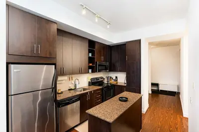 a kitchen with wooden cabinets and a stainless steel refrigerator at Luxury 1BR Plus Den Condo With Sauna Access in Toronto