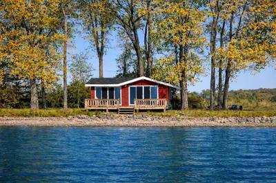 a red cabin on the shore of the water at Sandbanks Beach Cottage in West Lake