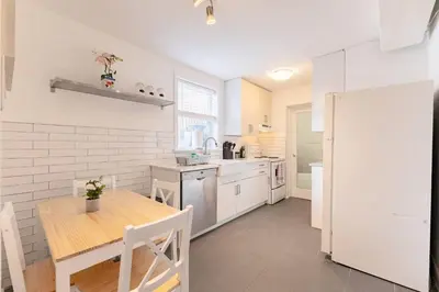 a white kitchen with a wooden table and a dining room at 2min to DT, Cowboys, Full-Kitchen, 65 inch TV in London