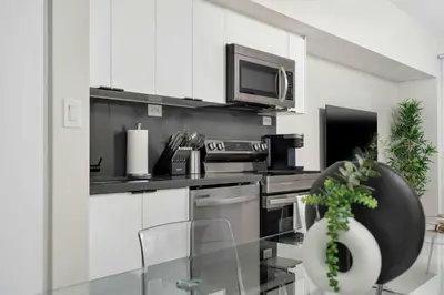 a kitchen with white cabinets and a microwave and a tv at Modern CityPlace 2BR Balcony & Free Parking in Toronto