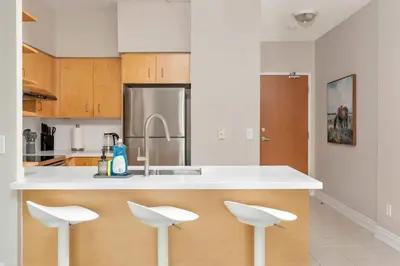 a kitchen with white counter tops and white stools at Bright 1BR Suite with Patio & CN Tower Views in Toronto
