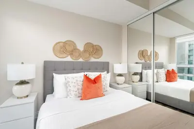 a bedroom with two beds with orange pillows and mirrors at Bright 1BR Suite with Patio & CN Tower Views in Toronto