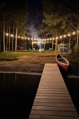 a dock with a boat on the water at night at Waterfront Muskoka Cottage with FirePit, BBQ and Canoes in Bracebridge