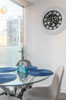 a glass table with chairs and a clock on the wall at Modern Studio Condo High Floor Downtown Toronto in Toronto