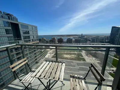 a balcony with two wooden chairs and a view of the city at RivetStays - Dan Leckie Suite in Toronto