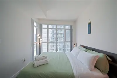 a bedroom with a bed with a large window at Skyline Stays Chic 2BR Steps from Everything in Toronto