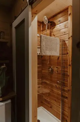 a bathroom with a shower with a wooden wall at Woodrush Cabin a Charming Lakefront Tiny Cabin in Victoria Road