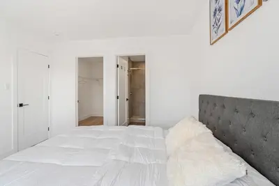 a white bedroom with a large bed with a gray headboard at Modern 3BR House, King, 2 Queens, Parking in London