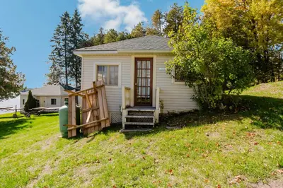 a small white house on a grass field at Charming Lakeview Family Resort in Katchwanooka with Private BBQ and firepit in Lakefield