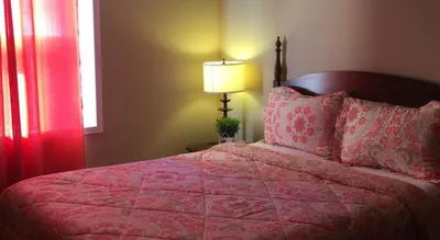 a bedroom with a bed with a red blanket and a lamp at The Falls Family Lodge in Niagara Falls