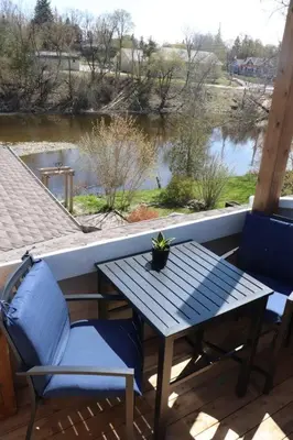 a table and chairs on a porch with a view of a river at Etherington Suites in Elora