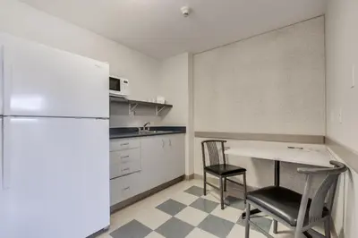a kitchen with a table and two chairs and a refrigerator at Residence & Conference Centre - Niagara-on-the-Lake in Niagara on the Lake