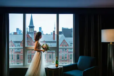 a bride standing in front of a window with a bottle of wine at The Yorkville Royal Sonesta Hotel Toronto in Toronto