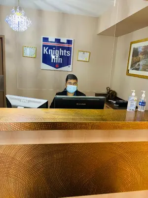 a person wearing a mask sitting at a desk with a laptop at Knights Inn Orillia in Orillia