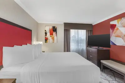 a bedroom with a white bed and a flat screen tv at Best Western Plus Rose City Suites in Welland