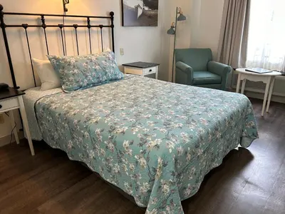 a bedroom with a bed with a green blanket and a chair at The Village Inn of Lakefield in Lakefield