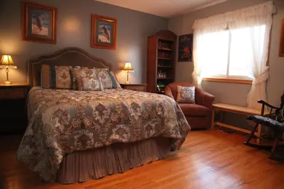 a bedroom with a bed and a chair and a window at A Garden Stroll Bed & Breakfast in Stratford