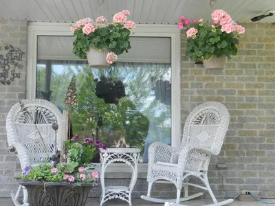 three wicker chairs and a table on a porch with flowers at A Garden Stroll Bed & Breakfast in Stratford