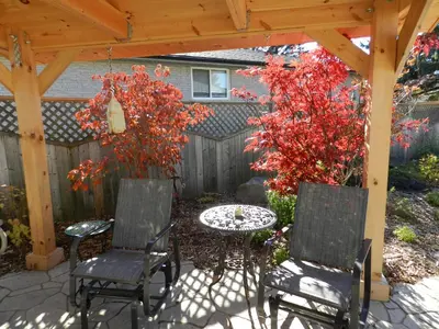 a patio with a table and chairs under a wooden pergola at A Garden Stroll Bed & Breakfast in Stratford