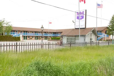 a building with a fence in front of a field at Knights Inn Lindsay in Lindsay