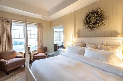 a bedroom with a large white bed and a chair at The Inn at Cobble Beach in Kemble