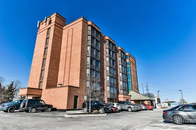 a tall brick building with cars parked in a parking lot at Best Western Plus Cambridge Hotel in Cambridge