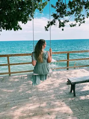 a woman sitting on a swing by the ocean at The Lakeside Prince Edward County in Wellington